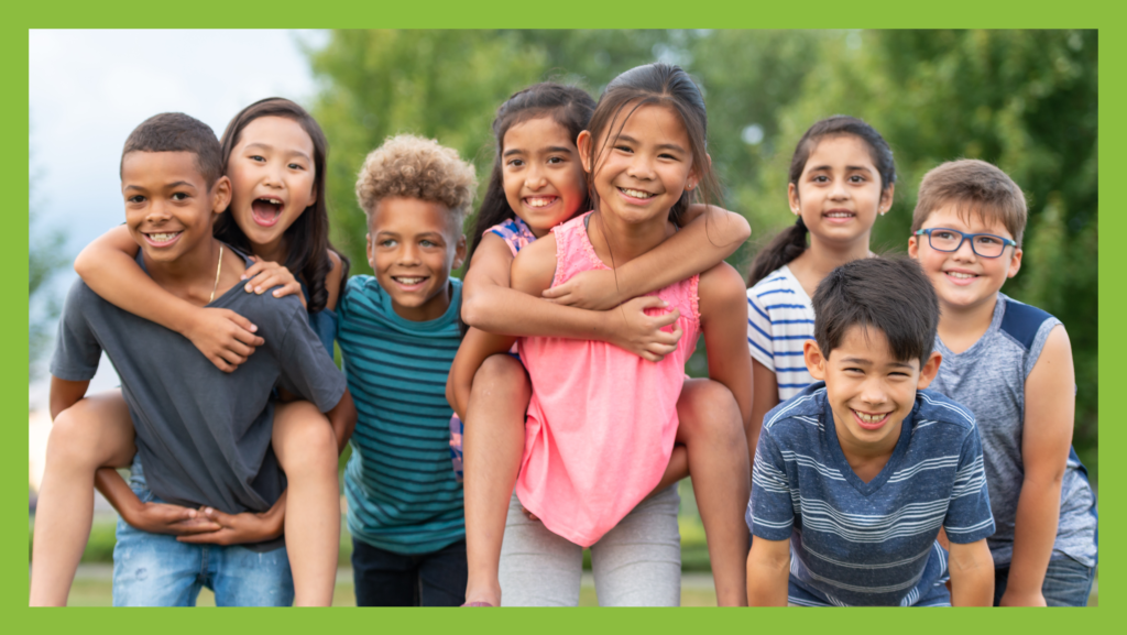 A group image of children. They are standing close together and some children are piggy-backing others. The children are diverse and happy.